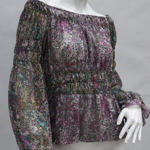 May include: A floral print off-the-shoulder blouse. The sheer fabric features a pattern of small flowers in shades of pink, green, and purple on a dark background. The blouse has long sleeves with ruffled cuffs and a gathered waist.