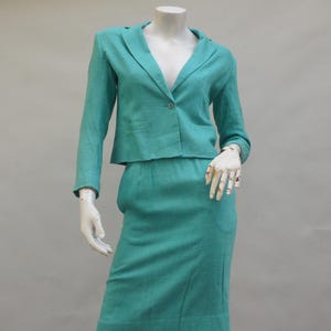 May include: A teal blue skirt suit with a cropped blazer and a skirt that falls to the knee. The suit is made of a soft, textured fabric.