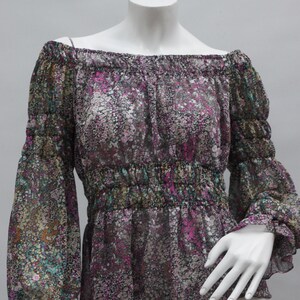 May include: A floral print off-the-shoulder blouse. The sheer fabric features a pattern of small flowers in shades of pink, purple, green, and brown. The long sleeves have elastic cuffs, and the waist is cinched with elastic.