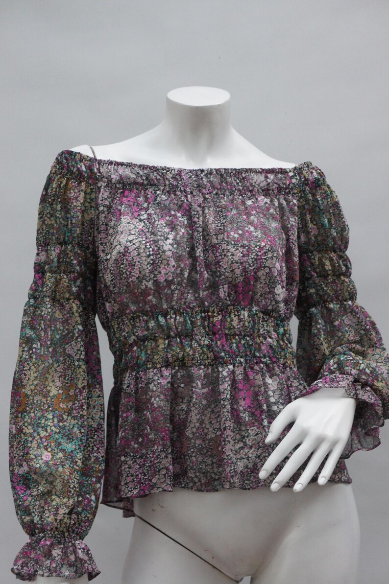 May include: A floral print off-the-shoulder blouse. The sheer fabric features a pattern of small flowers in shades of pink, purple, green, and brown. The long sleeves have elastic cuffs, and the waist is cinched with elastic.