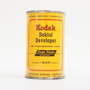 Peut inclure: Une boîte de révélateur Kodak Dektol vintage. La boîte cylindrique est jaune avec du texte rouge et noir, dont "Kodak Dektol Developer" et "Single Powder". La boîte est conçue pour des usages photographiques et pour faire 1 litre (946 ml).