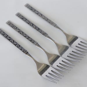 May include: Four stainless steel forks with decorative handles. The handles feature a black and silver scroll design. The forks are arranged diagonally on a white surface, showcasing their tines and overall design.