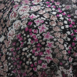 May include: Close-up of a fabric with a floral pattern. The design features small, clustered flowers in shades of pink, white, and brown against a black background. The fabric appears to be lightweight and slightly sheer.