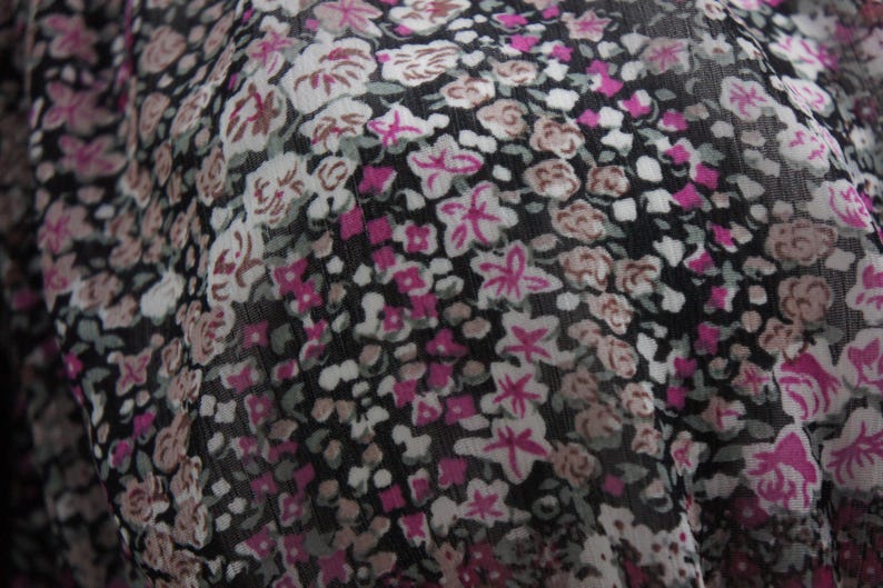 May include: Close-up of a fabric with a floral pattern. The design features small, clustered flowers in shades of pink, white, and brown against a black background. The fabric appears to be lightweight and slightly sheer.