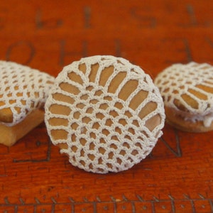 May include: Three white crocheted doilies on top of wooden knobs. The doilies are a delicate, lacy design.