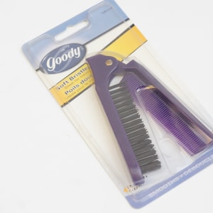 Peut inclure: Une brosse à cheveux Goody violette avec des poils doux et un peigne. L'emballage indique "Soft Bristles Great for Tangles Poils doux Démêle tous les types de cheveux" et "Smooths + De-tangles".