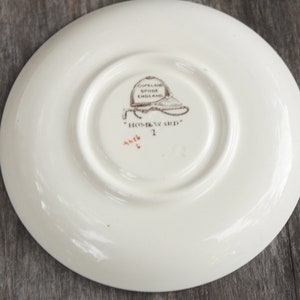 Puede incluir: Plato de cer&aacute;mica blanco con una imagen marr&oacute;n y negra de un sombrero y el texto "Copeland Spode England" y "Homward" en la parte inferior.
