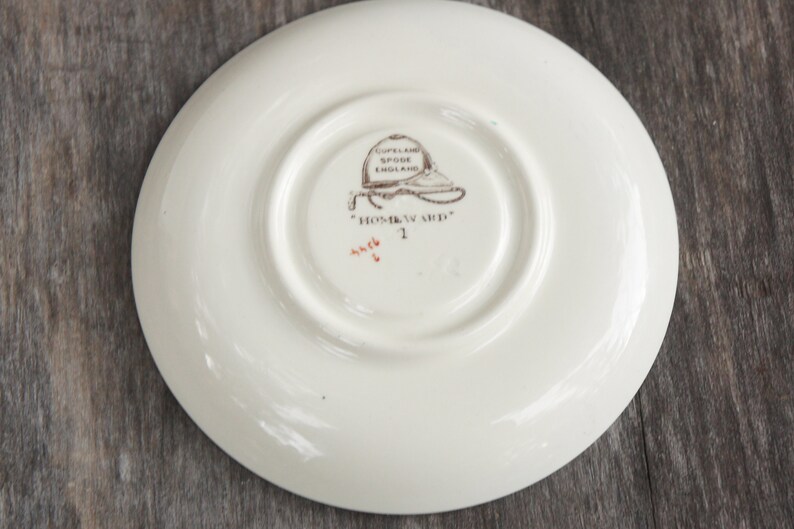 Puede incluir: Plato de cer&aacute;mica blanco con una imagen marr&oacute;n y negra de un sombrero y el texto "Copeland Spode England" y "Homward" en la parte inferior.