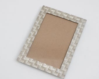 May include: Silver rectangular picture frame with a woven texture. The frame has a neutral-colored backing and is set against a white background. This decorative frame is suitable for displaying photographs or artwork.