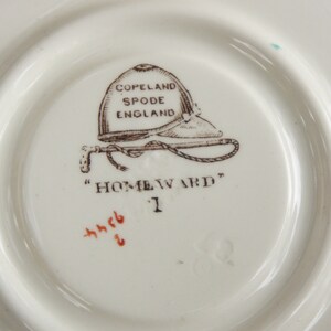 Puede incluir: Un platillo de cer&aacute;mica blanca con un dise&ntilde;o impreso en marr&oacute;n de un casco de montar a caballo y un l&aacute;tigo. El texto "COPELAND SPODE ENGLAND" y "HOMEWARD" est&aacute; impreso en el platillo.