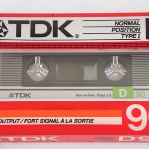 Puede incluir: Un paquete de cinta de casete rojo, blanco y verde con el texto "TDK" y "D 90" impreso en &eacute;l. La cinta de casete est&aacute; etiquetada como "Posici&oacute;n Normal Tipo I" y "Alta Salida/Se&ntilde;al Fuerte a la Salida".