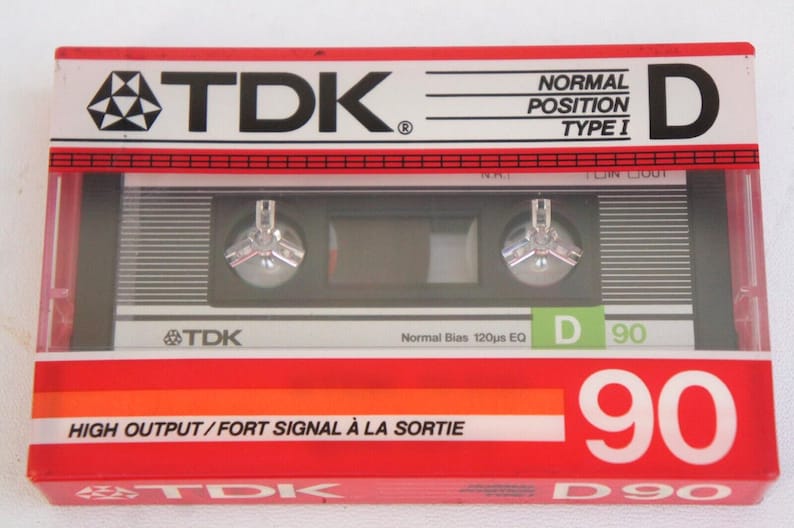 Puede incluir: Un paquete de cinta de casete rojo, blanco y verde con el texto "TDK" y "D 90" impreso en &eacute;l. La cinta de casete est&aacute; etiquetada como "Posici&oacute;n Normal Tipo I" y "Alta Salida/Se&ntilde;al Fuerte a la Salida".