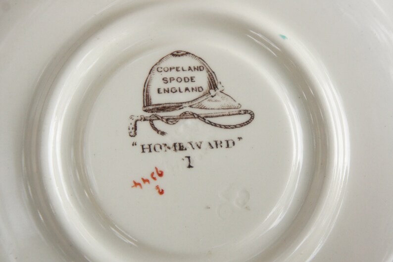 Puede incluir: Un platillo de cer&aacute;mica blanca con un dise&ntilde;o impreso en marr&oacute;n de un casco de montar a caballo y un l&aacute;tigo. El texto "COPELAND SPODE ENGLAND" y "HOMEWARD" est&aacute; impreso en el platillo.