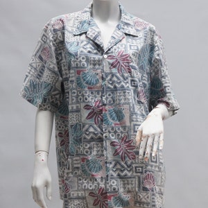 以下が含まれることがあります： 幾何学模様と花柄のボタンダウン半袖シャツ。 シャツは襟付きでマネキンに着せられています。 パターンには、貝殻、葉、幾何学模様の形が、グレー、ティール、マルーンの色合いで含まれています。