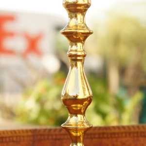 May include: A pair of gold metal candle holders with a classic design. The holders have a round base and a tall, slender stem with a decorative, fluted design.