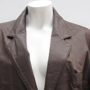 May include: A brown leather blazer with a notched lapel and a single-breasted design. The jacket has a classic tailored fit and a pocket on the front. The blazer is displayed on a white mannequin.