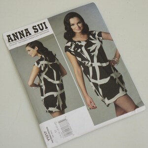 May include: A black and white patterned dress sewing pattern by Anna Sui. The pattern features a short-sleeved dress with a geometric design.