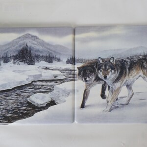 May include: Two square ceramic tiles featuring a winter landscape. One tile shows a snowy river and mountains, the other depicts two wolves in the snow. The tiles are predominantly grey, white, and brown.