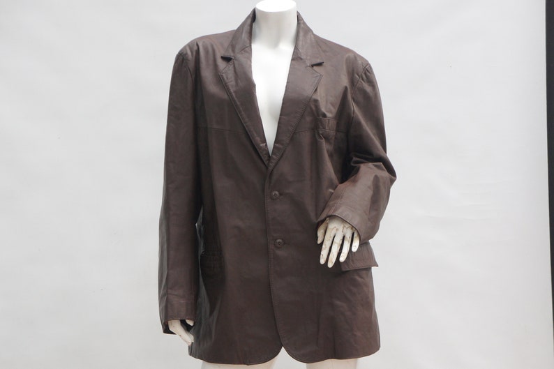 May include: A brown blazer with a two-button closure and two front pockets. The blazer is displayed on a mannequin against a white background. The jacket has a classic lapel and long sleeves.