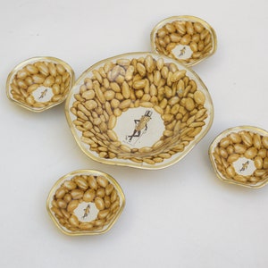 Peut inclure: Un ensemble de cinq plats de service vintage sur le thème des cacahuètes. Les plats présentent un motif de cacahuètes et un personnage de dessin animé au centre. Les bords sont dorés et les plats sont disposés sur une surface blanche.