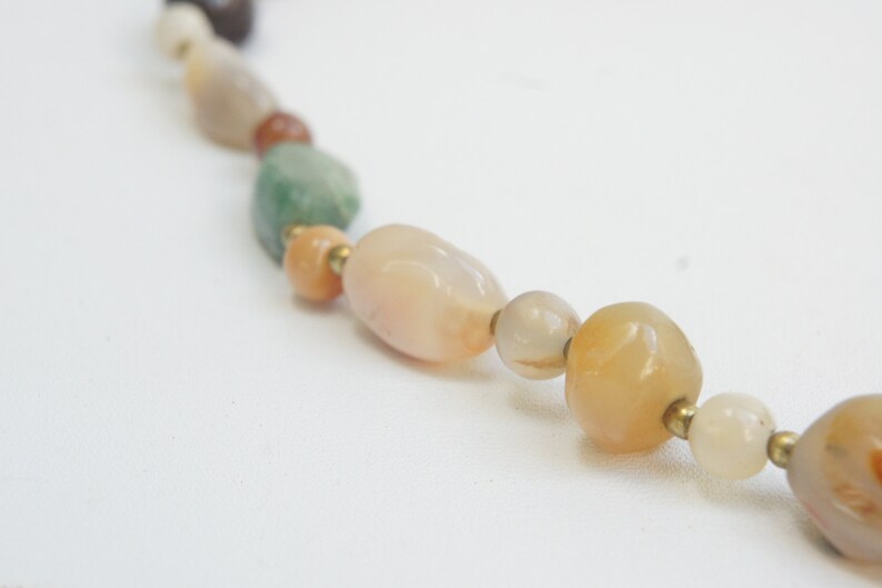May include: A close-up of a multi-colored gemstone necklace with various shades of brown, green, and orange. The necklace is made of smooth, rounded beads.