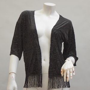 May include: A black, open-front cardigan with a textured pattern and fringe trim.