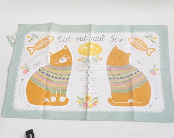 May include: A light blue and white fabric panel with a cat design. The orange cats wear colorful sweaters and are next to fish illustrations. Text reads "Cut out and Sew" and "Create the Cutest".