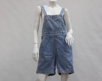 May include: Light blue denim overall shorts. The shorts feature adjustable straps, a bib pocket, and side pockets. The garment is displayed on a mannequin against a plain white background. The denim has a faded, worn appearance.