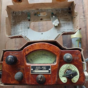 May include: A vintage brown and tan radiation detector with a gauge, knobs, and a dial. The device has a rectangular shape with a hinged top and a label that reads "ДП-5Б". The dial has numbers from 0.1 to 200.