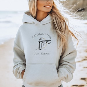 Può includere: Una felpa con cappuccio bianca con una grafica in bianco e nero di un faro e il testo "Southampton Light Keeper".