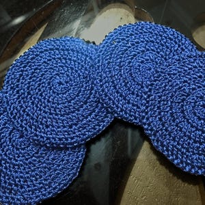 Puede incluir: Cuatro posavasos de ganchillo azul con un patrón en espiral. Los posavasos están hechos de un hilo suave y texturizado.