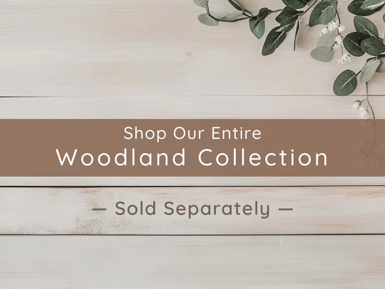 May include: A rectangular brown banner with white text that reads Shop Our Entire Woodland Collection and Sold Separately, positioned over a light-colored wooden surface with a sprig of green eucalyptus leaves in the upper right corner.