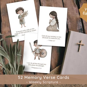Puede incluir: Un conjunto de 52 tarjetas de versículos de memoria con escritura semanal, con ilustraciones de acuarela de niños y una Biblia con una cruz. Las tarjetas tienen versículos bíblicos. Las palabras "YEAR Edition" están en una etiqueta dorada.