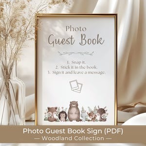 May include: A vertical rectangular sign in a gold frame featuring the text Photo Guest Book, instructions 1. Snap it. 2. Stick it in the book. 3. Sign it and leave a message, and a line of illustrated woodland animals including a bear and fox.