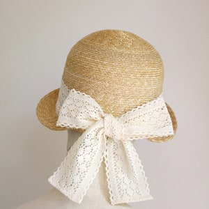 A straw hat with a wide brim and a large white lace bow tied at the back.