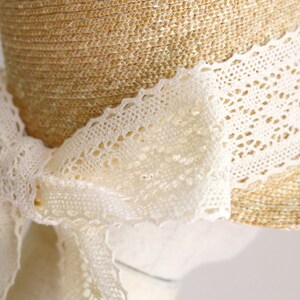 A straw hat with a wide brim and a white lace trim. The lace is tied in a bow at the back of the hat.