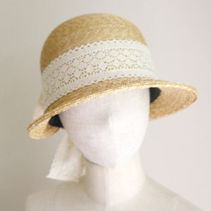 A straw hat with a wide brim and a white lace trim. The hat is sitting on a white mannequin head made by Grosgrain