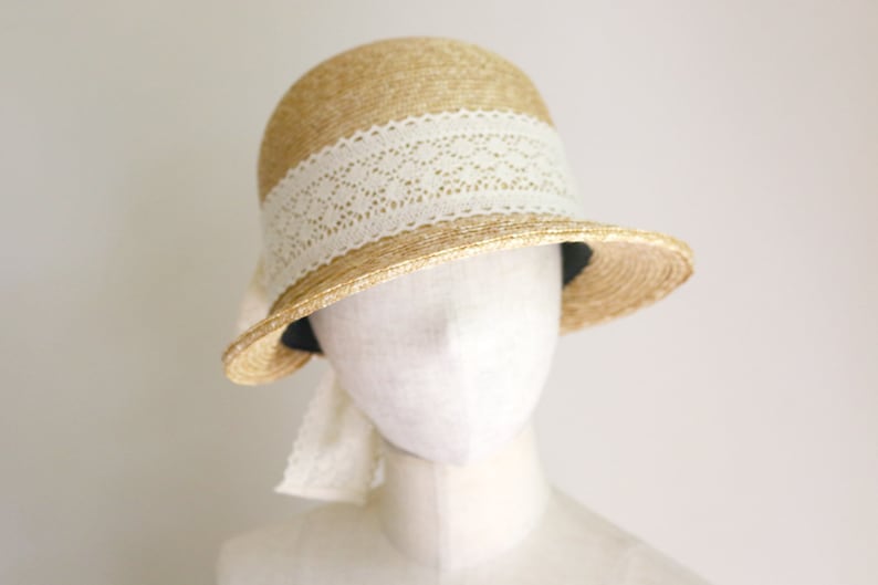 A straw hat with a wide brim and a white lace trim. The hat is sitting on a white mannequin head made by Grosgrain