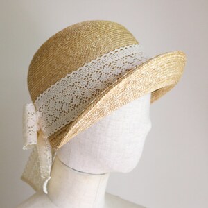 A straw hat with a white lace trim and a bow. The hat is on a white mannequin head.