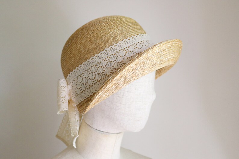 A straw hat with a white lace trim and a bow. The hat is on a white mannequin head.