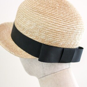 A straw hat with a wide brim and a black ribbon around the crown. The ribbon has a large bow on the back