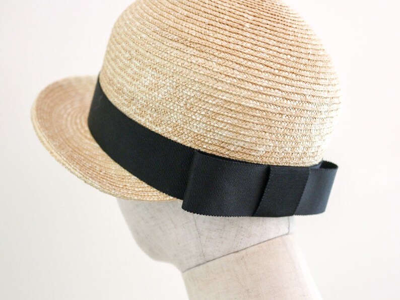 A straw hat with a wide brim and a black ribbon around the crown. The ribbon has a large bow on the back