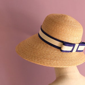 May include: A straw sun hat with a wide brim and a navy blue and white ribbon tied in a bow.