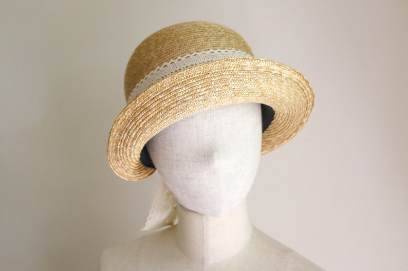 A straw hat with a wide brim and a white lace ribbon. The hat is beige and the ribbon is white. Made by Grosgrain