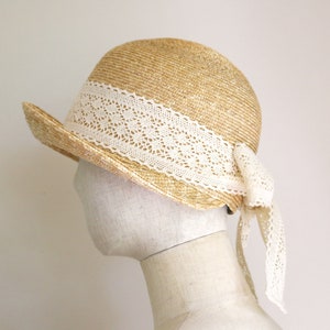 A straw hat with a wide brim and a white lace trim. The hat has a bow at the back.