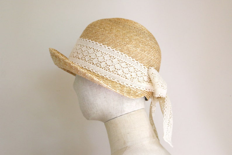 A straw hat with a wide brim and a white lace trim. The hat has a bow at the back.
