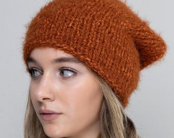 May include: A close-up of a woman wearing a fuzzy, burnt orange beanie. The beanie is knit and has a slouchy fit.