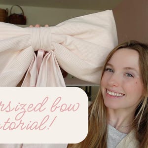 K&ouml;nnte beinhalten: Eine Frau h&auml;lt einen gro&szlig;en, rosa-wei&szlig; gestreiften Bogen hoch. Der Bogen ist &uuml;berdimensioniert und hat ein schlichtes Design. Der Text "Oversized bow tutorial!" ist in rosa auf wei&szlig;em Hintergrund geschrieben.