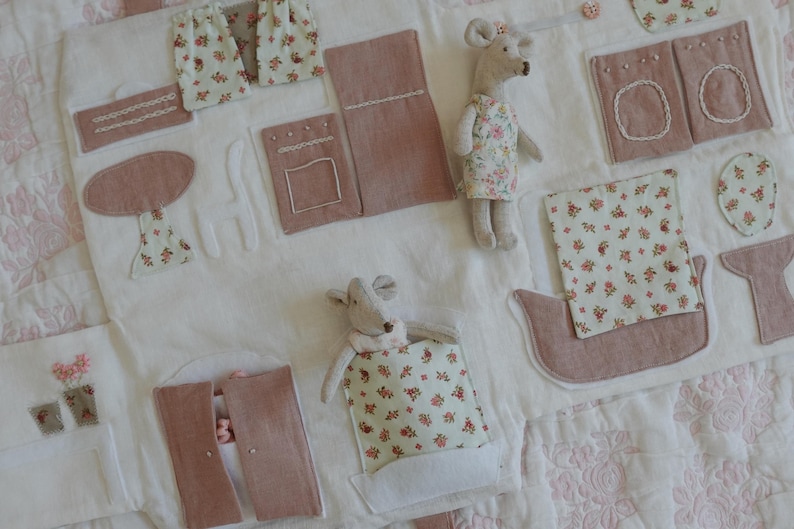 Puede incluir: Un tapete de juego hecho a mano con un dise&ntilde;o caprichoso. Presenta varias aplicaciones de tela en tonos rosa y blanco, incluyendo cortinas en miniatura, una mesa y un barco. Tambi&eacute;n hay dos peque&ntilde;as mu&ntilde;ecas de rat&oacute;n.