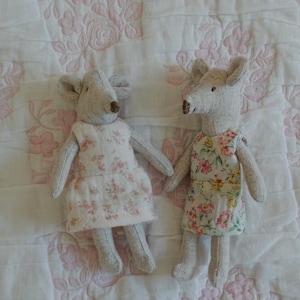 Puede incluir: Dos mu&ntilde;ecas de rat&oacute;n hechas a mano. Cada mu&ntilde;eca es gris con orejas grandes y un hocico largo. Una ratona viste un vestido blanco con estampado floral rosa, la otra viste un vestido floral con flores rosas, amarillas y verdes.